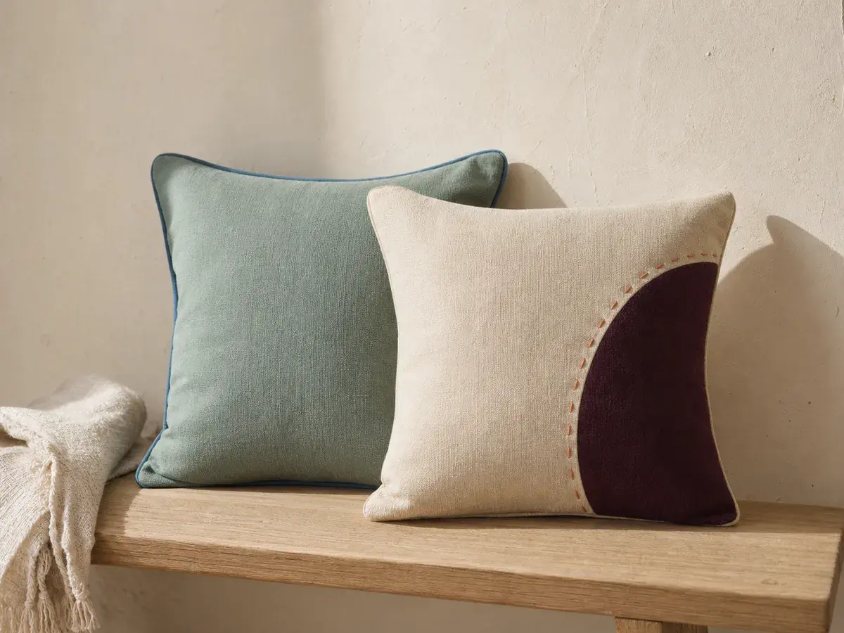 Concept cream and muted jade decorative cushion covers on a natural wood bench